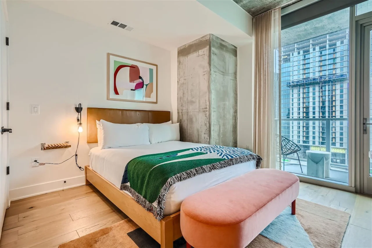 Studio bedroom with a green bedcover, pink bench and tall windows